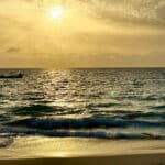 Golden sunset over the Atlantic Ocean with gentle waves reaching the sandy beach